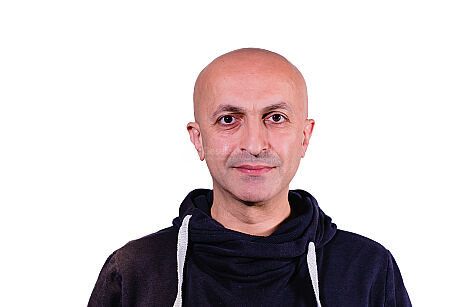 Portrait von einem lächelnden Hamza vor einem weißen Hintergrund.