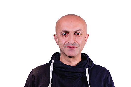 Portrait von einem lächelnden Hamza vor einem weißen Hintergrund.