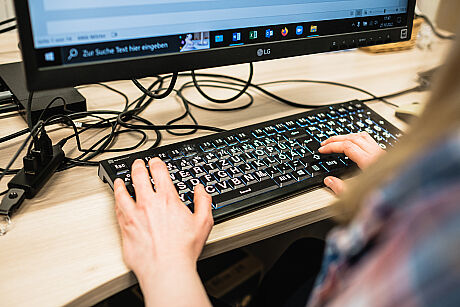  Zwei Hände auf einer Tastatur mit größeren, weißen Buchstaben.  