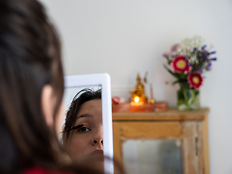 Beyond The Frame: Junge Perspektiven auf Vielfalt im Glauben - Frau schminkt sich vor Hausschrein des tibetischen Buddhismus